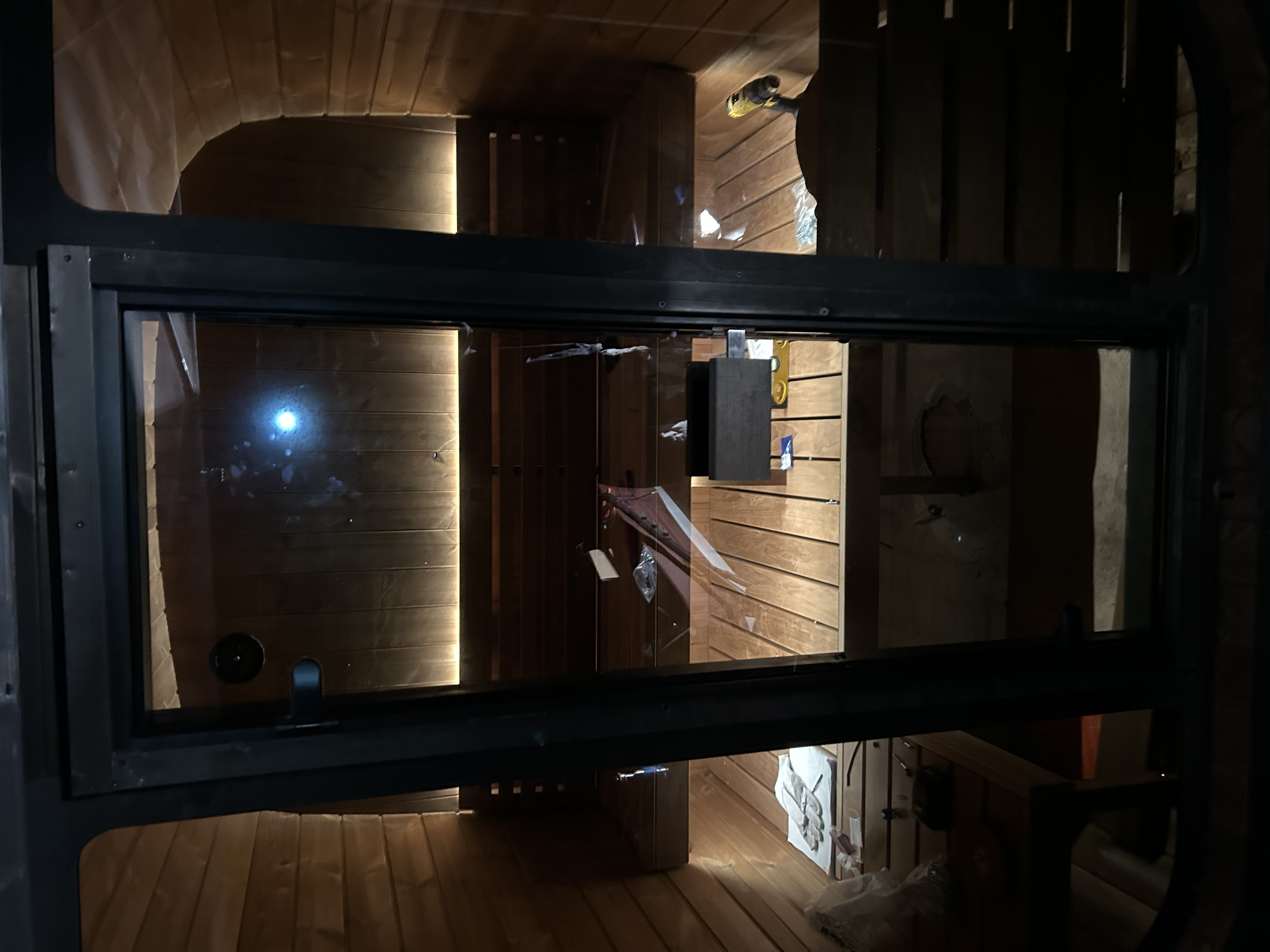 Interior view of a wooden barrel sauna under construction with warm backlighting and tools on the benches.