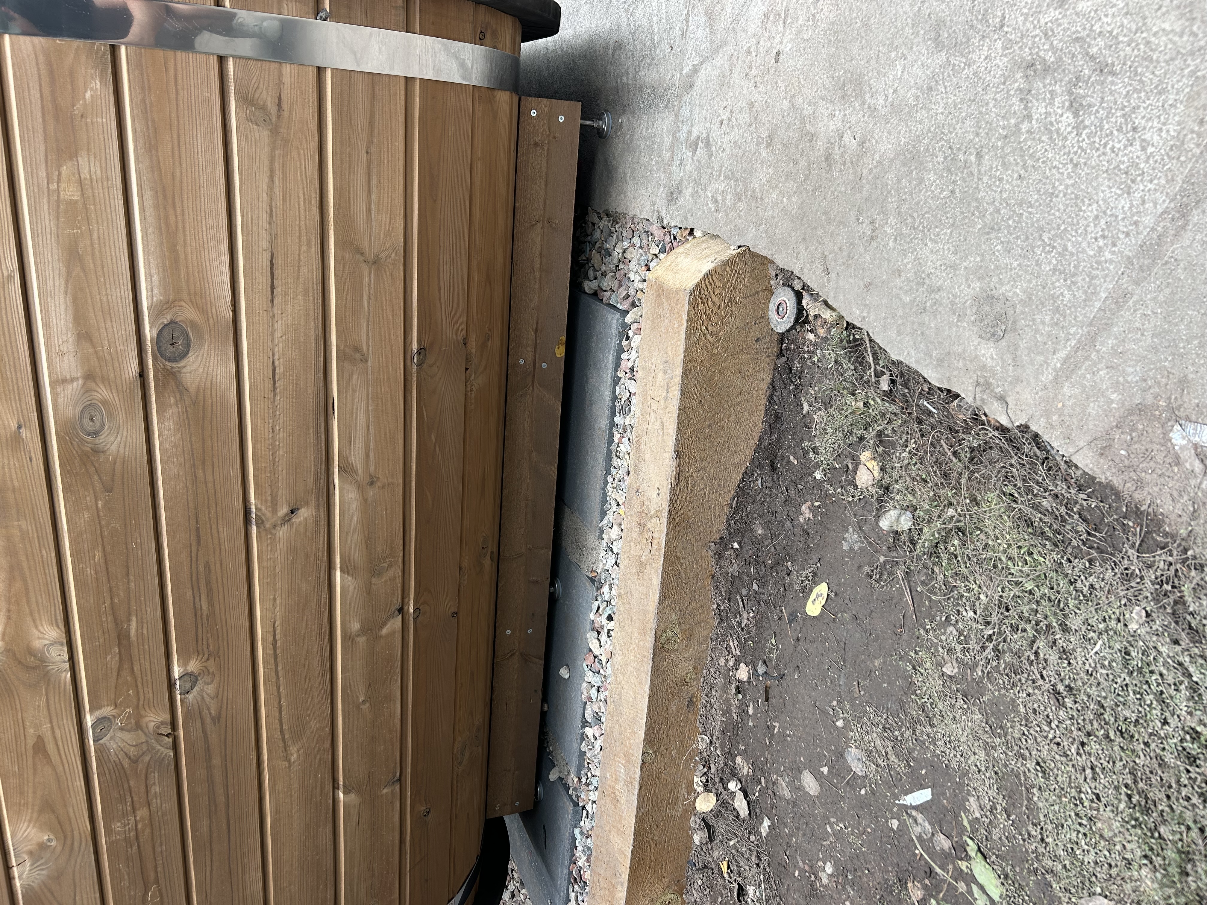 Close-up of wooden sauna base with metal leveling feet resting on patio pavers and gravel.